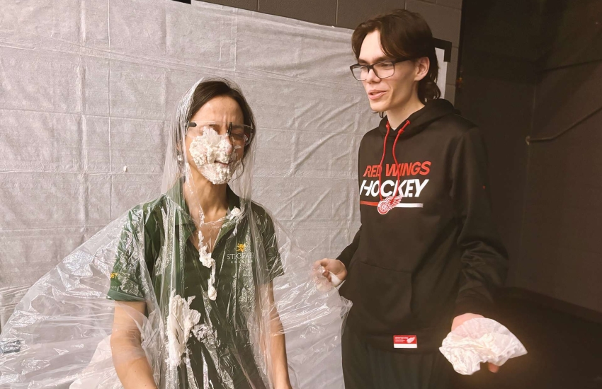 Katrina Tomanelli laughs at the fresh layer of whipped cream student William Bradford applied during the 'pie your prof' fundraiser on Dec. 6, 2024. (Rich Garton/St. Clair College)
