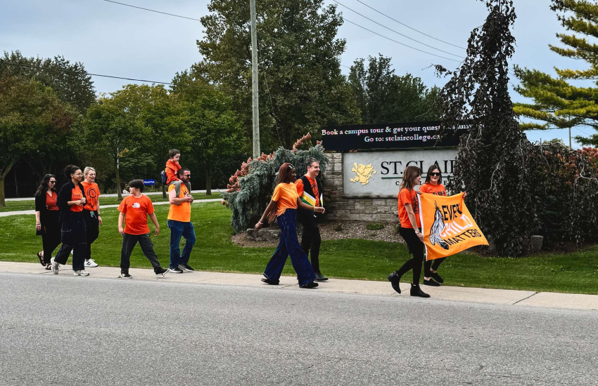 Students and staff at St. Clair College's Chatham Campus walk together in reflection on Orange Shirt Day