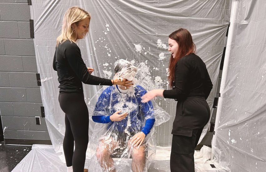 Two students hand deliver a pie into SSAA President George Karatzias' face