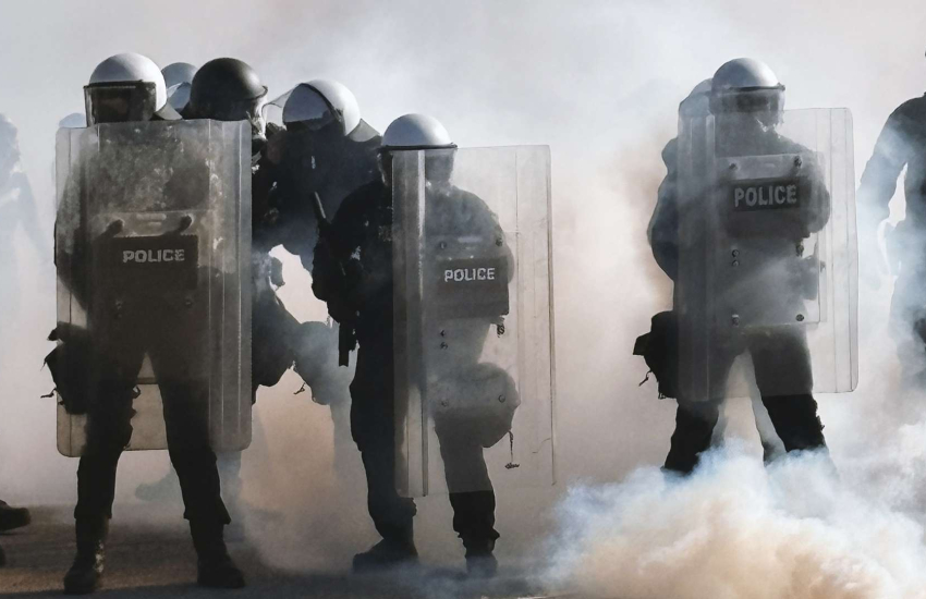 Police in riot gear surrounded by smoke