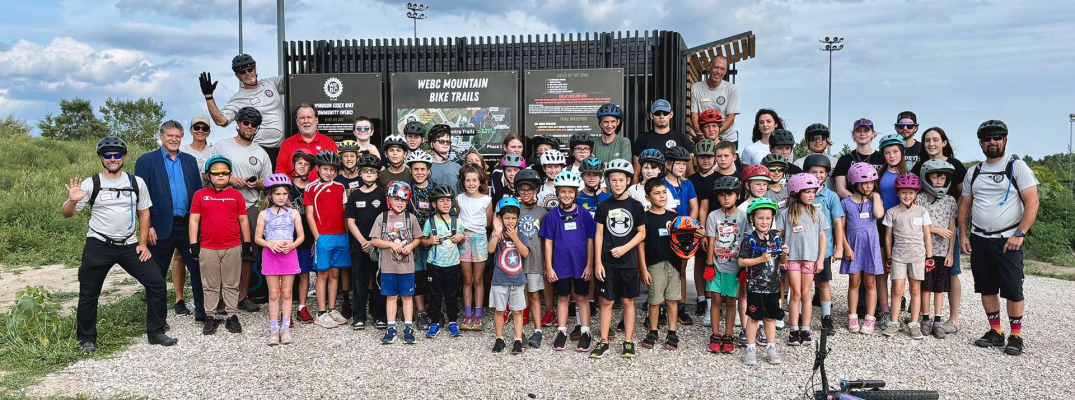 Members of the WEBC Youth Mountain Bike Club are joined by St. Clair College graduates and leadership for the unveiling of the new Libro Centre Bike Trails Kiosk in Amherstburg, Ont.