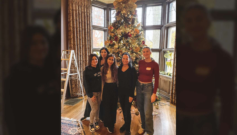 St. Clair College Interior Design students pose in front of a Christmas tree while decorating at Willistead Manor