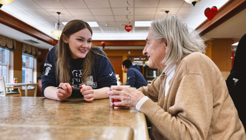 St. Clair College student Mckinley Lenehan sits down with a neighbour at Schlegel Villages' The Village at St. Clair for coffee and companionship