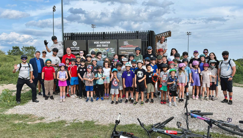 Members of the WEBC Youth Mountain Bike Club are joined by St. Clair College graduates and leadership for the unveiling of the new Libro Centre Bike Trails Kiosk in Amherstburg, Ont.