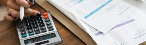 Fingers on calculator next to papers.