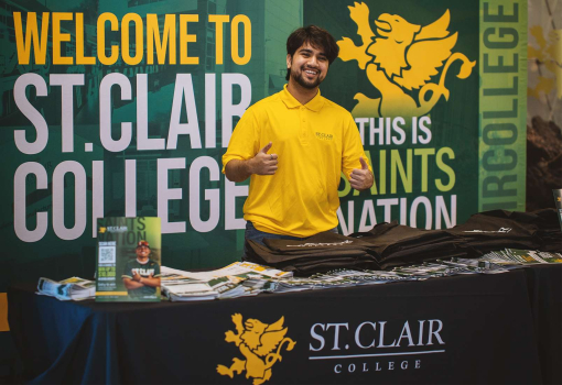 Person standing behind a desk, outfitted with St. Clair College gear.