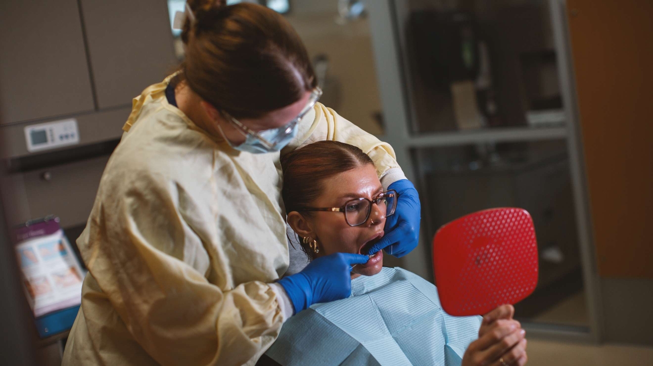 Hygienist flossing the teeth of a patient while she watches while looking at reflection in a mirror she's holding